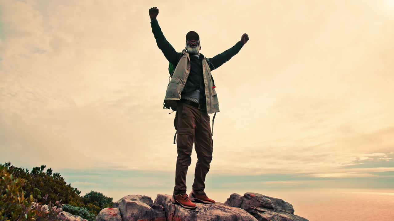 A man with a backpack celebrating on top of a mountain