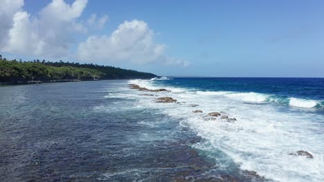 drone shot, ocean waves breaking on coral reefs by green tropical island