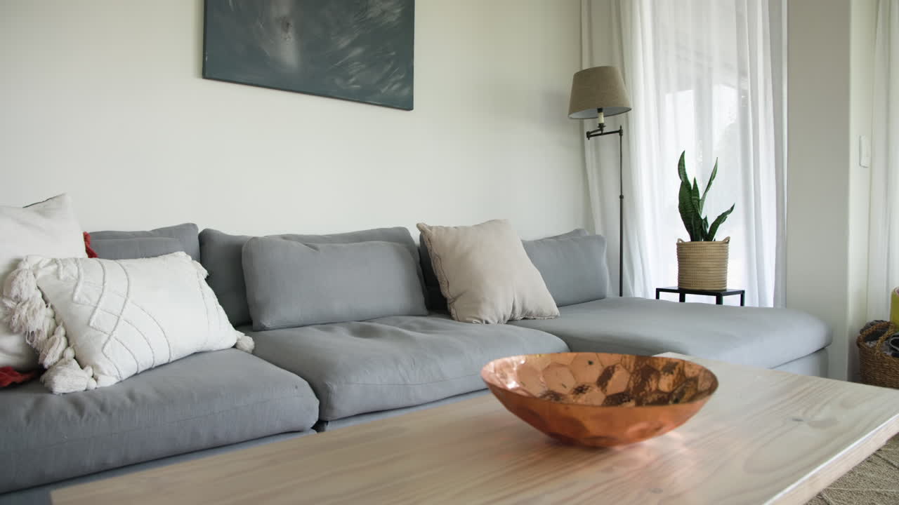 Cozy living room with gray sofa, decorative pillows, and copper bowl on table, copy space