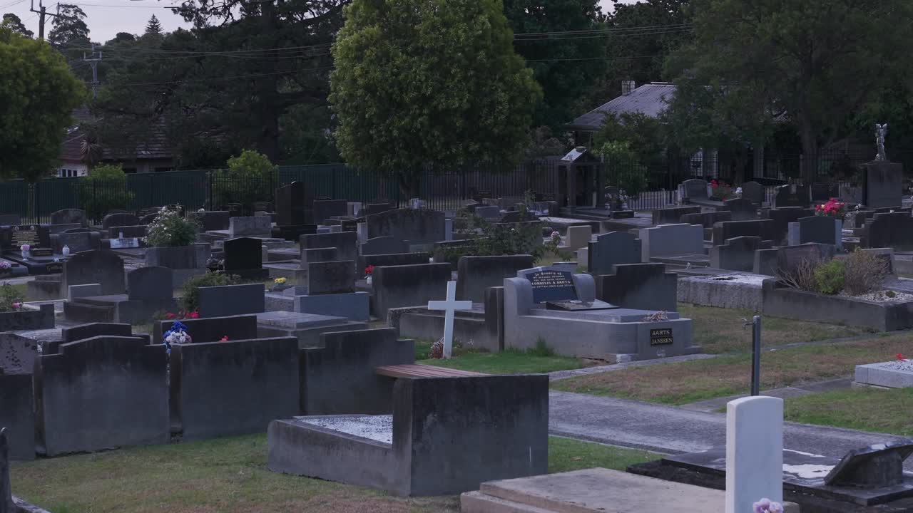 Video drone che riprende un cimitero sereno al tramonto a Ferntree Gully, Melbourne. L'ambientazione tranquilla presenta file di lapidi e vegetazione lussureggiante sotto un cielo crepuscolare.