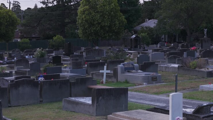 Video drone che riprende un cimitero sereno al tramonto a Ferntree Gully, Melbourne. L'ambientazione tranquilla presenta file di lapidi e vegetazione lussureggiante sotto un cielo crepuscolare.