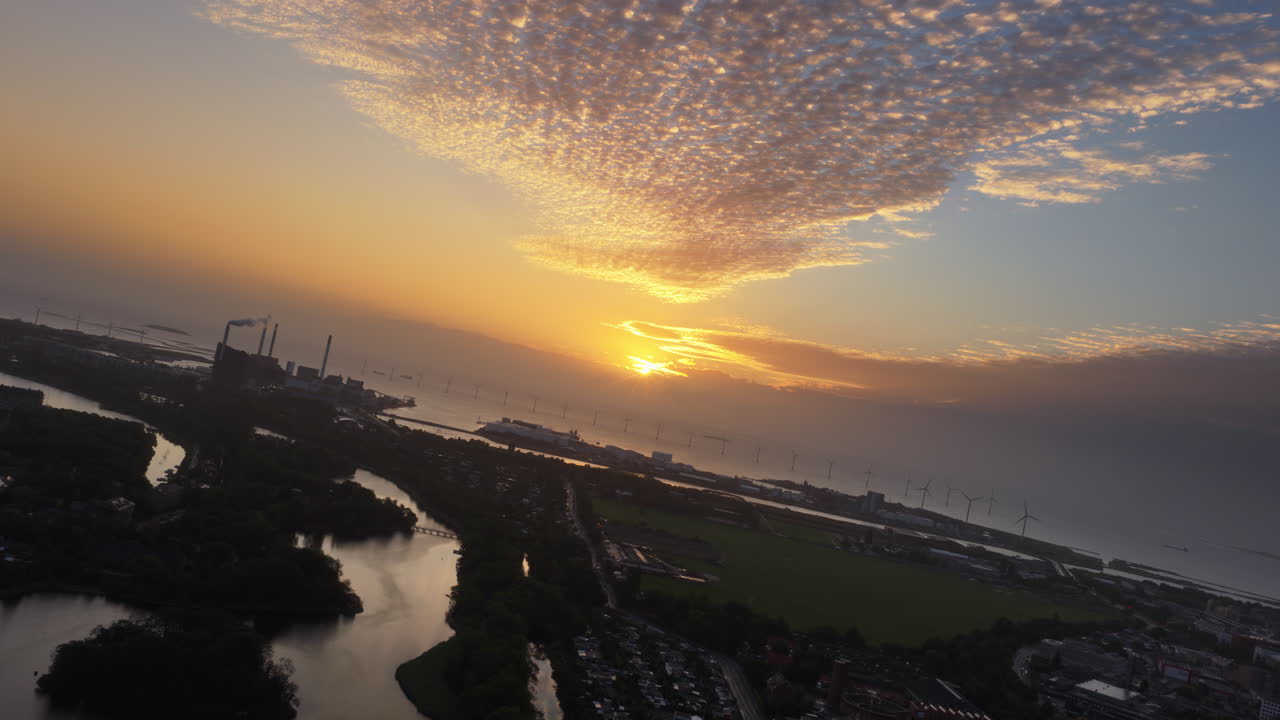 Aerial drone view of Copenhagen, Denmark at sunset with glowing skies, wind turbines in the background