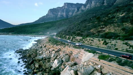 Costa-áspera-Y-Rocosa-Cerca-De-La-Bahía-De-Campamentos-Con-Automóviles-Circulando-Por-La-Carretera-Costera