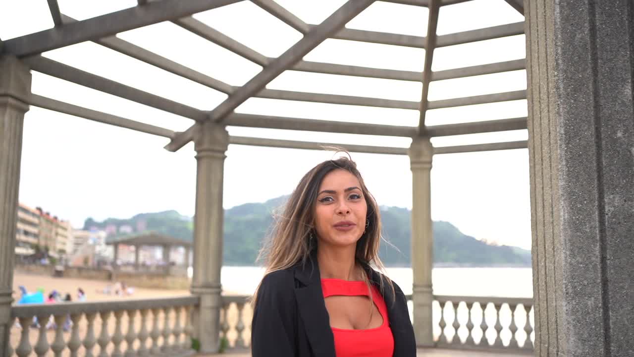 Woman in red dress and black blazer near the coast