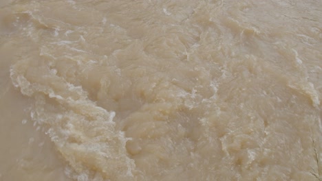 Tilt-up-shot-of-a-flooded-creek-with-muddy-brown-water-and-strong-current---Kentucky