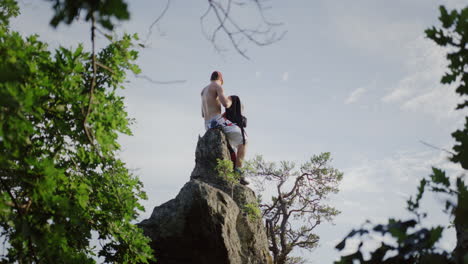 tipo bebiendo de una botella de agua en una roca grande en un paisaje de montaña, fondo cielo azul, árbol verde en primer plano, toma amplia cinematográfica, disfrutando de la naturaleza, hombre guapo, modelo masculino caucásico, clima soleado