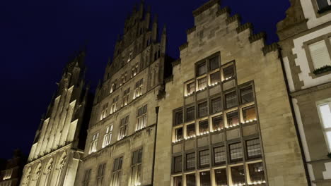 Statischer-Tiefwinkelschuss-Von-Alten-Historischen-Gebäuden-Des-Mittelalters-Mit-Lichtern-Im-Fenster-Vor-Dunklem-Himmel-Im-Hintergrund