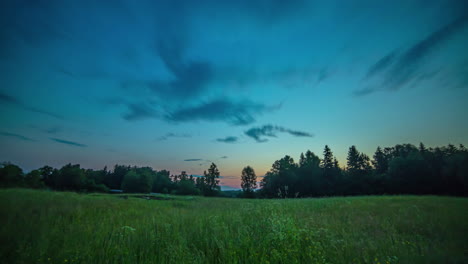 low angle view grassland with trees silhouette during sunrise, clouds crossing blue sky, time lapse