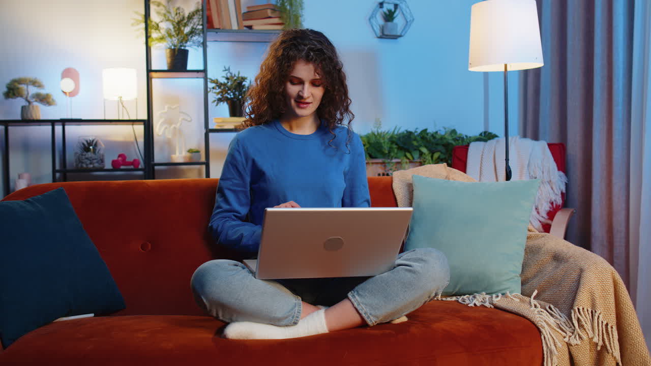 Happy woman opening laptop and working remotely sitting beside corgi dog on sofa at home room