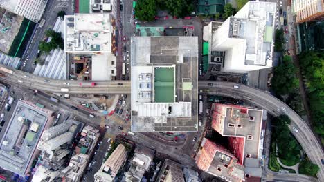 Tráfico-Que-Pasa-Por-Un-Edificio-De-Aparcamiento-En-El-Centro-De-Hong-Kong,-Con-Mega-Edificios-De-La-Ciudad,-Vista-Aérea