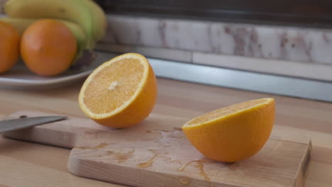 fresh orange sliced in half moving sideways back and forth on wooden chopping board