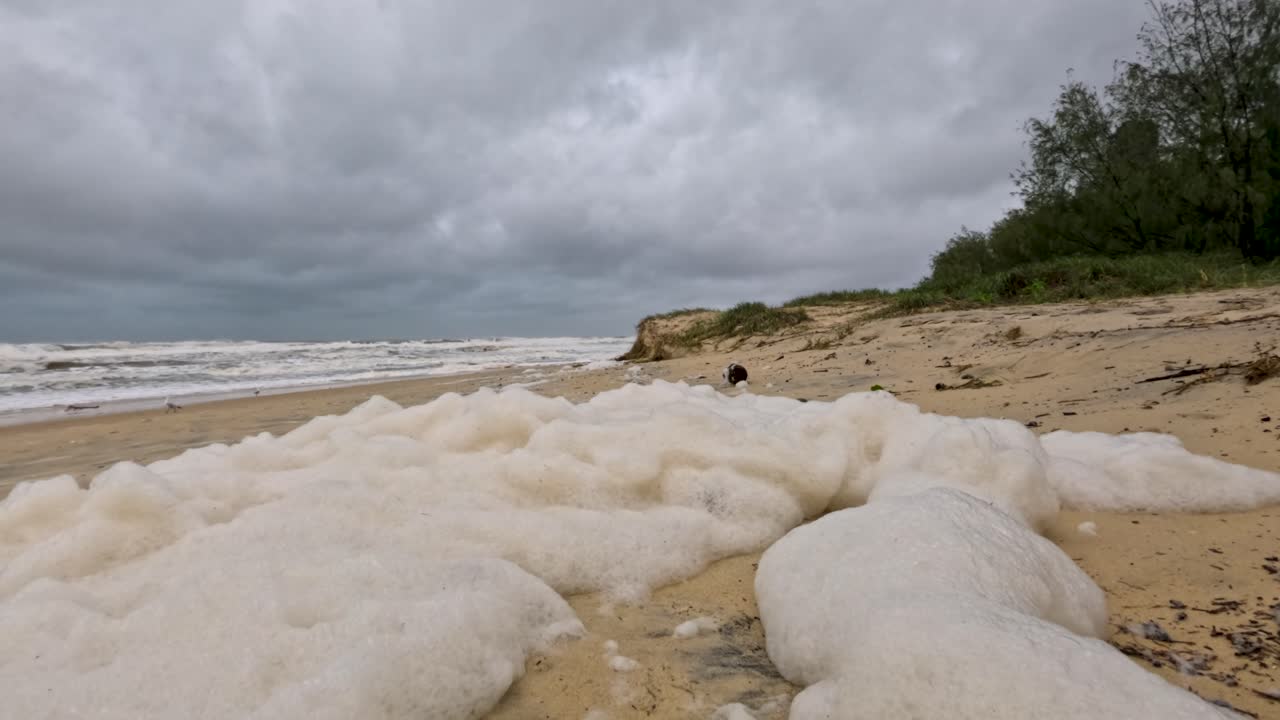 бурная пляжная сцена с пенными волнами, вымывающими на берег под облачным небом, захватывая сырую силу природы и воздействие загрязнения