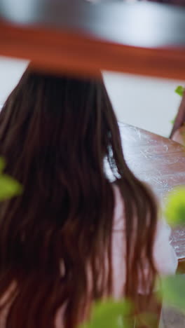 primer plano de marco de madera con hojas decorativas, con vista trasera de la dama sentada en la mesa usando su teléfono, una bolsa de compras a su lado, en un entorno interior acogedor y moderno