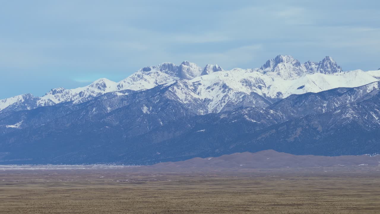 Una ripresa aerea laterale segue le aspre montagne Sangre de Cristo e le Great Sand Dunes in Colorado. Questa prospettiva invernale cattura la portata epica delle cime innevate e del terreno arido.