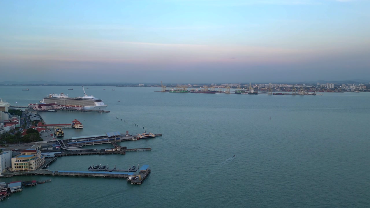 George Town Penang port area at dawn or dusk, showing city buildings, a cruise ship docked, ferries, and water. Great aerial view speed ramp hyper motion time lapse ascending raise up panorama drone