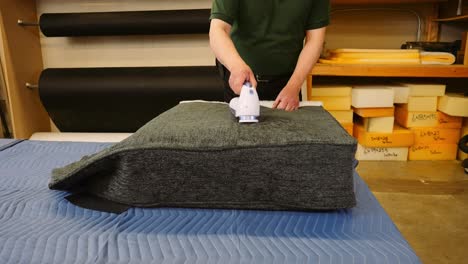 a furniture repair carpenter uses an electric fabric shaver machine to repair an upholstery sofa cushion in a workshop