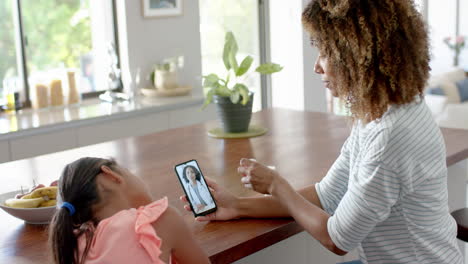 biracial mother and sick daughter having smartphone video call with female doctor, slow motion