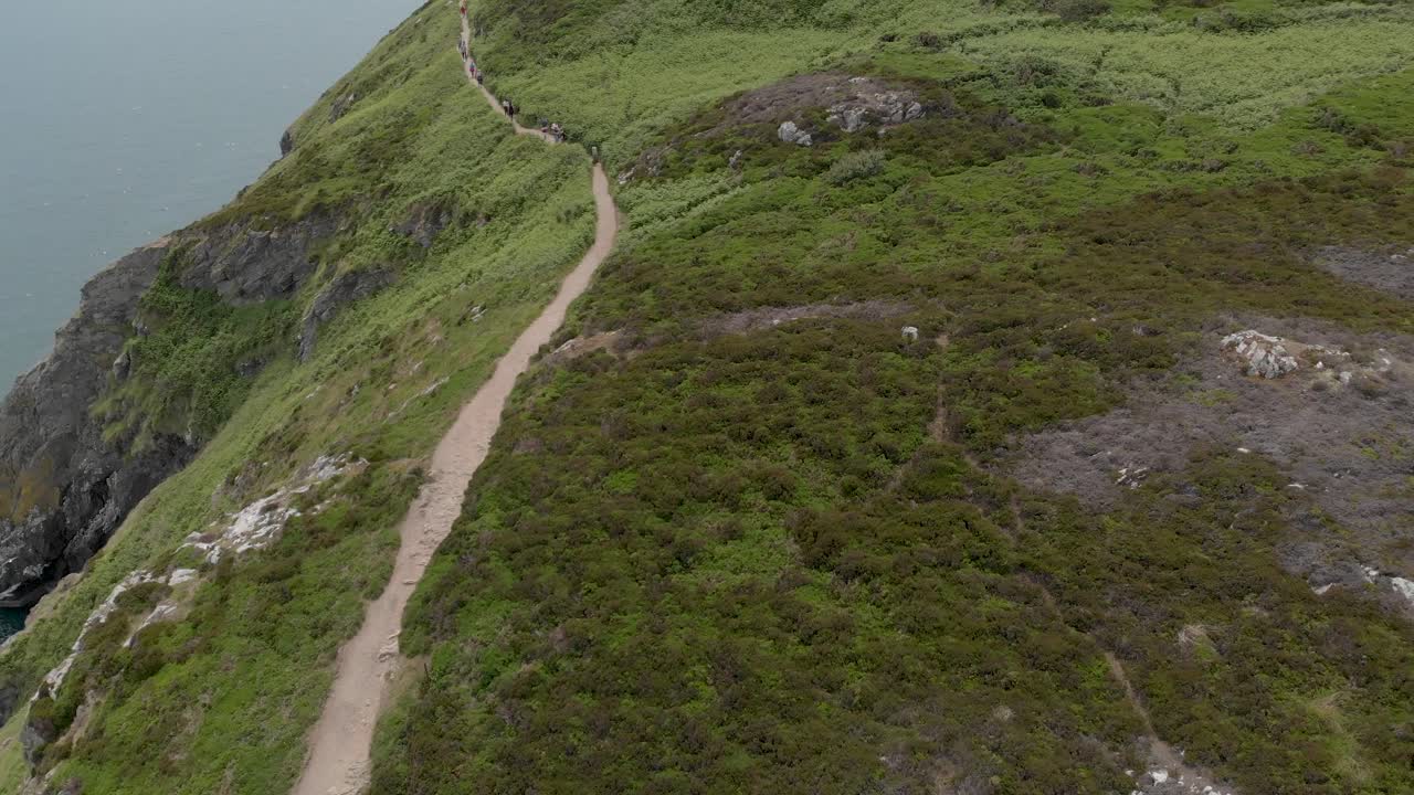 Turisti che camminano su un sentiero vicino all'oceano su una montagna in una giornata di sole.