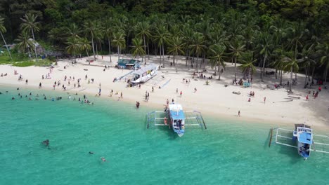 personas en la playa tropical de siete comandos nadando en aguas cristalinas con barcos turísticos y palmeras en el fondo, el nido