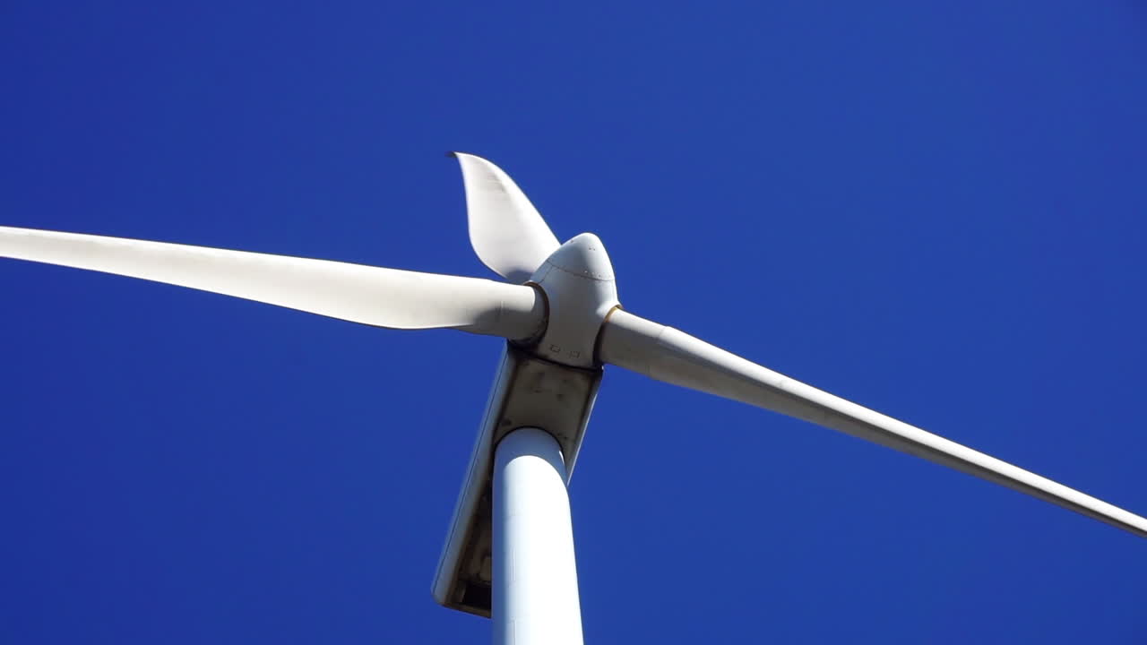 Close-up view of a wind turbine's blades spinning against a blue sky background