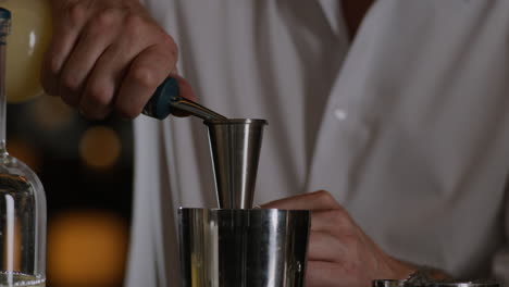 closeup shot of a bartender measuring liquor into a jigger and pouring it into a metal shaker