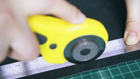 person cuts leather cloth with yellow rotary cutter closeup