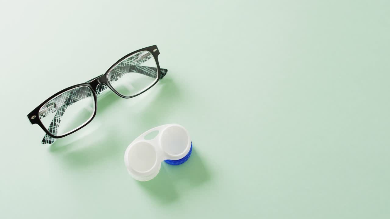 Video of pair of glasses and contact lenses case on green background with copy space