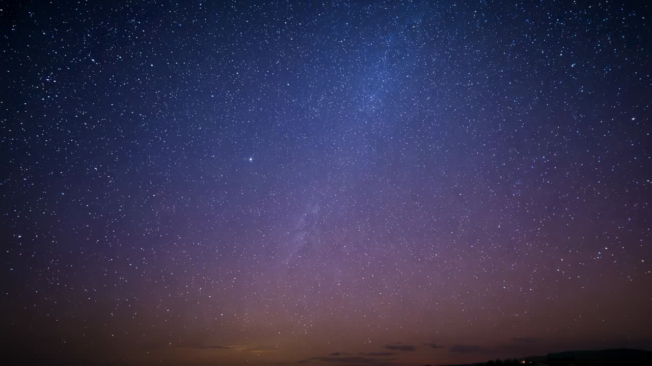 Tweaking camera revealing Milky Way and stars brightening above remote horizon with orange glow