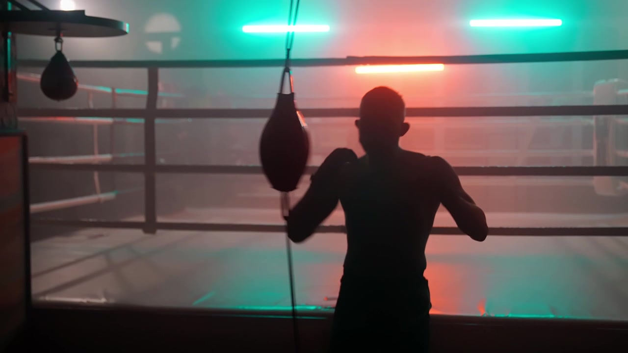 Silhouette di un pugile maschio che si allena con il sacco veloce in una palestra buia.