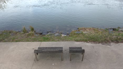 top high angle view of two benches on concrete sidewalk overlooking peaceful river