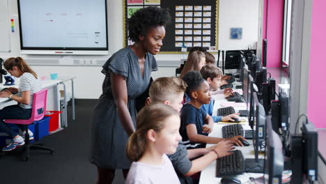 Teacher Helping Male Pupil In Line Of High School Students Working at Screens In Computer Class