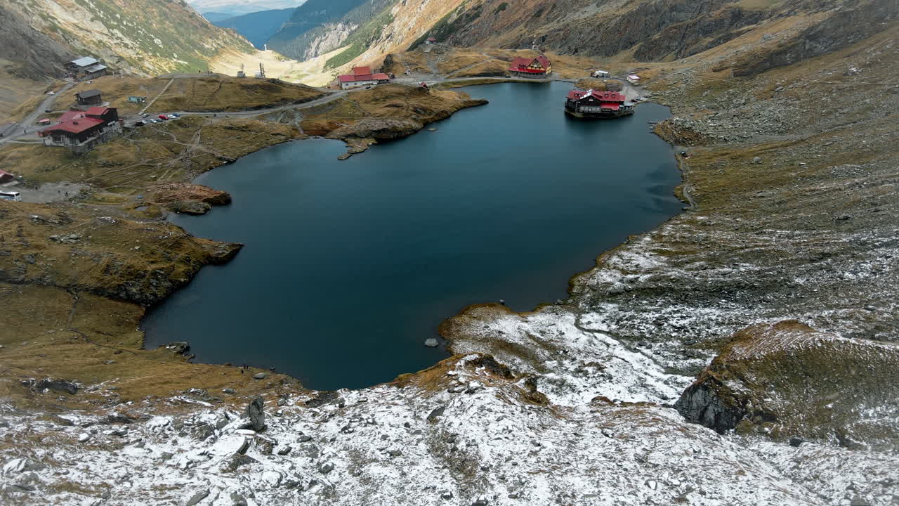 Aerial drone view of nature in Romania. Transfagarasan route in Carpathian mountains, Balea Lake resort and rocky slopes covered with snow, valley, clouds