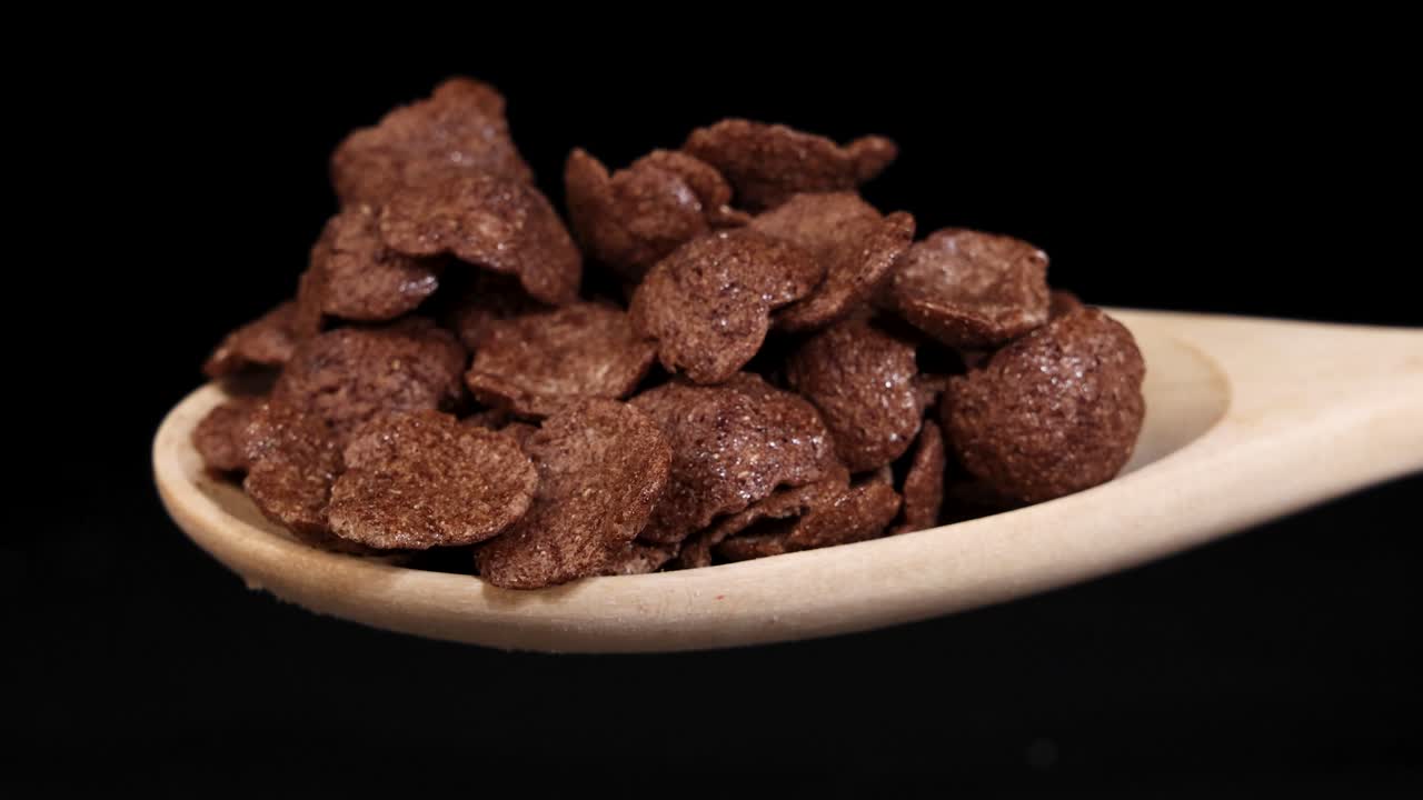 Chocolate cereal pieces tumble from a wooden spoon against a black background, captured in a dynamic sequence
