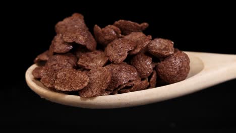 chocolate cereal pieces tumble from a wooden spoon against a black background, captured in a dynamic sequence