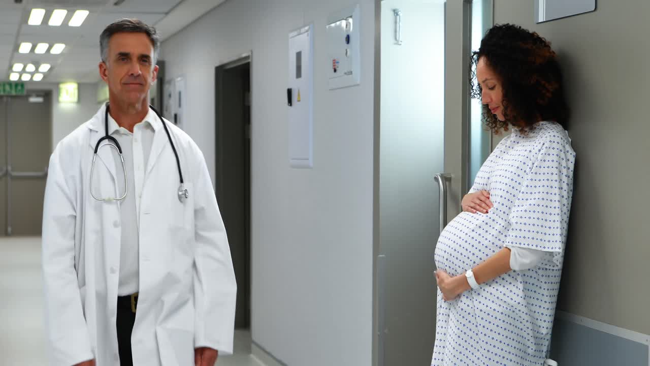 Pregnant woman touching her belly while doctor walking in corridor