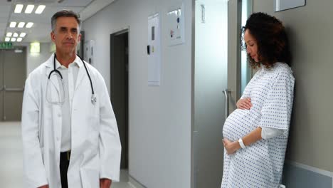 pregnant woman touching her belly while doctor walking in corridor