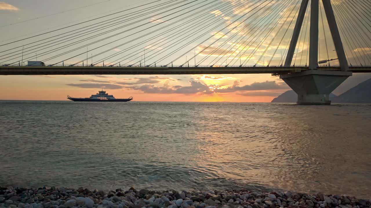 Sunset over the sea with a ferry passing under a bridge
