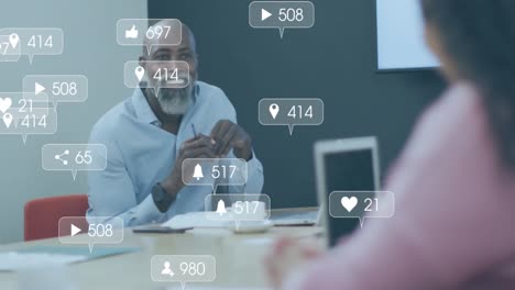 Animation-Von-Social-Media-Symbolen-Vor-Einem-Afroamerikanischen-Mann,-Der-Mit-Einer-Kollegin-Im-Büro-Spricht