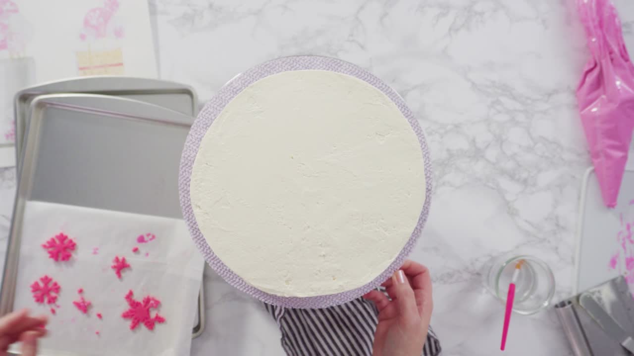 decorando el pastel funfetti redondo con copos de nieve de fondante rosado y blanco.