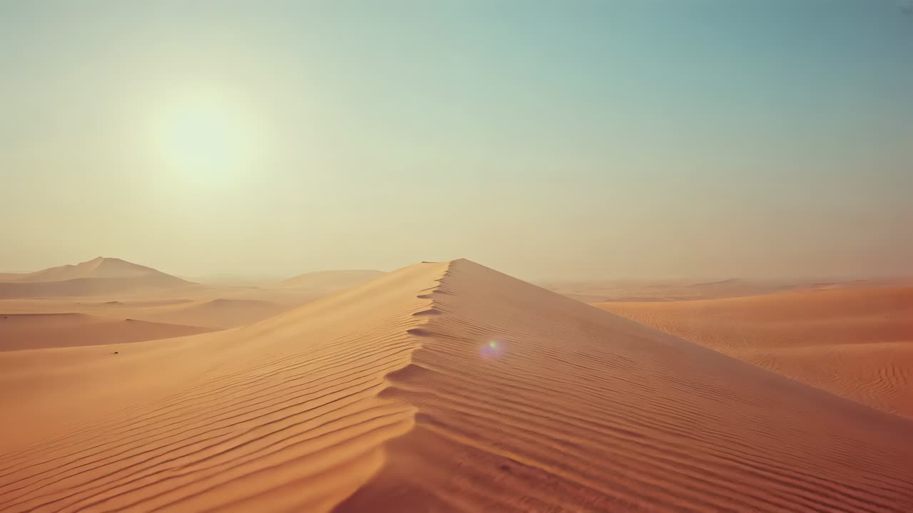 Drone con videocamera che inizia a sorvolare la cresta di una duna di sabbia su un crinale nel deserto, con riverbero solare che mostra le increspature