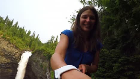 Frau-Lächelt-In-Die-Kamera,-Wasserfall-Im-Hintergrund-4k