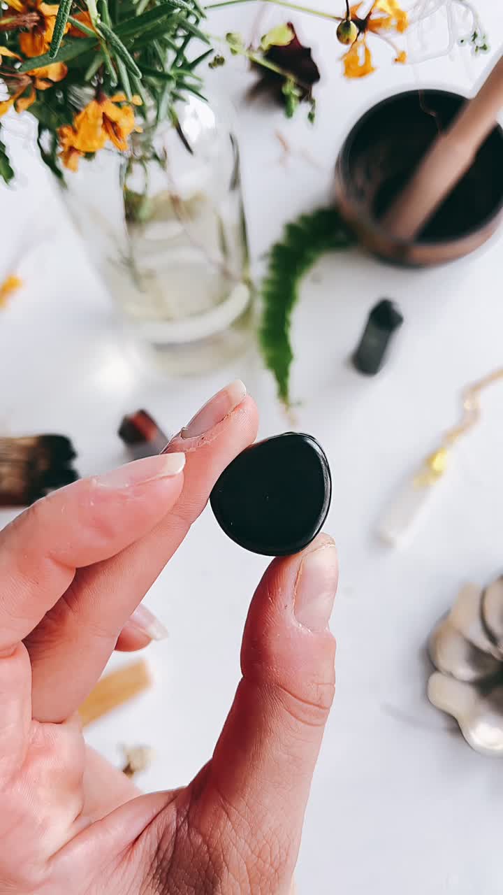 Hand holding a black obsidian crystal, surrounded by other crystals and nature-inspired items.