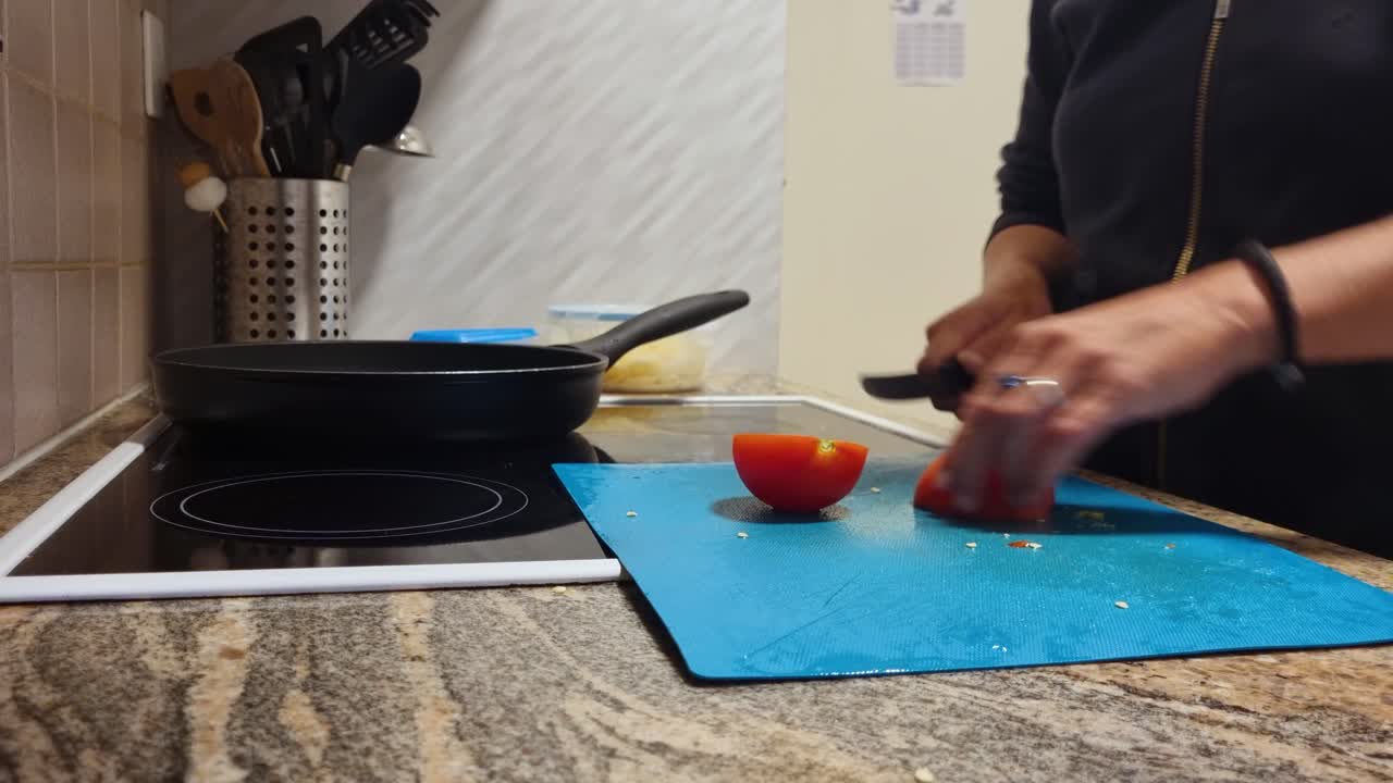 Close-up of a woman’s hands slicing a shiny red tomato on a blue cutting board in her home kitchen, preparing a wholesome vegetarian meal for her family, Swiss lifestyle