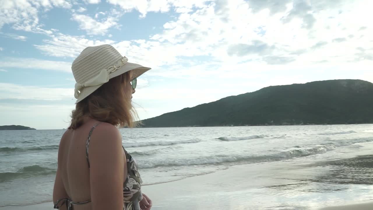 Happy young Latin American female white enjoys the beach on her vacations in Brazil. He has a hat and sunglasses.