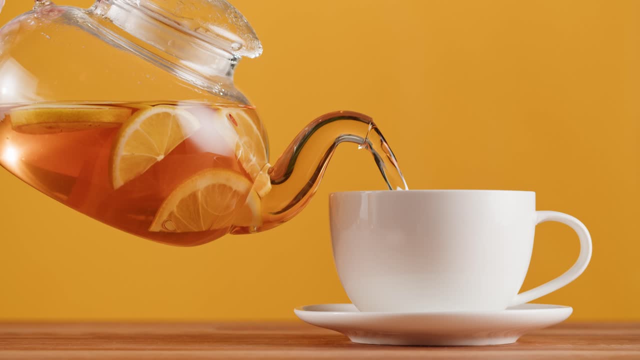 Pouring Hot Lemon Tea from a Glass Teapot into a White Cup
