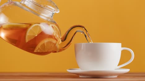 pouring hot lemon tea from a glass teapot into a white cup
