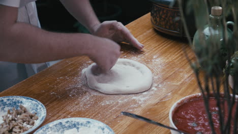 chef formando la masa de pizza a mano en forma circular en una mesa de cocina