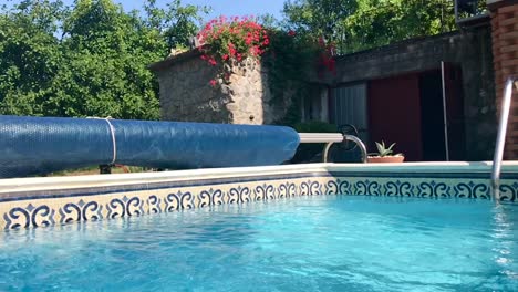 Scenic-swimming-pool-landscape-with-rustic-stone-house-and-blue-solar-cover-reel-in-slow-motion