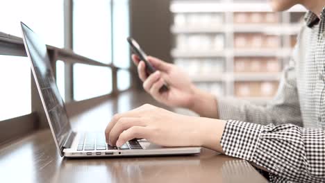 joven hombre de negocios asiático usando computadora portátil en el espacio de trabajo con teléfono inteligente y portátil en un escritorio de madera. mano masculina escribiendo en el teclado del portátil. estilo de vida independiente en el concepto de la era digital.
