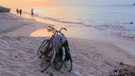 sunset shot along a beach with two bicycles parked on the shore and children playing in distance